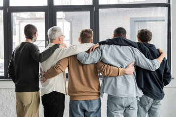 Back view of interracial men with alcohol addiction hugging in rehab center.