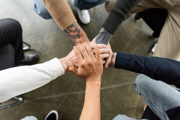 Top view of multiethnic people holding hands together during anonymous alcoholics meeting in rehab center.