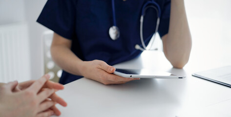 Doctor and patient sitting at the table in clinic while discussing something. The focus is on female physician's hands, close up. Medicine concept.