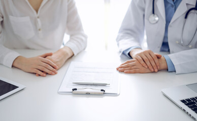 Doctor and patient discussing current health questions while sitting near of each other and using clipboard at the table in clinic, just hands closeup. Medicine concept.