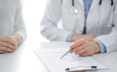 Doctor and patient discussing current health questions while sitting near of each other and using clipboard at the table in clinic, just hands closeup. Medicine concept.