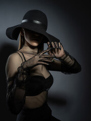 Fashion portrait of a young girl in a black bra and transparent top. Felt black hat. Model posing, faces not visible photo in studio.