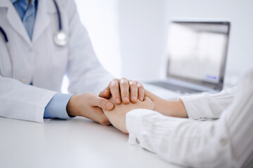 Doctor and patient sitting opposite each other at the table in clinic office. The focus is on female physician's hands reassuring woman, only hands, close up. Medicine concept. - 579819130