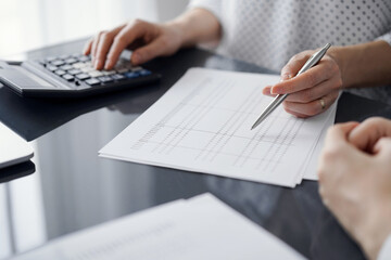 Fototapeta premium Woman accountant using a calculator and laptop computer while counting and discussing taxes with a client. Business audit and finance concepts.