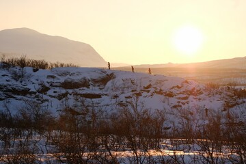 Silhouettes of tourists on snowshoes on island on lake Torneträsk (Tornestrask) around Abisko National Park (Abisko nationalpark) in sunset winter scenery. Sweden, Arctic Circle, Swedish Lapland