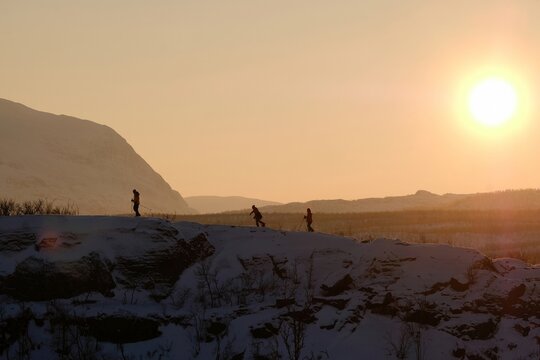 Silhouettes of tourists on snowshoes on island on lake Torneträsk (Tornestrask) around Abisko National Park (Abisko nationalpark) in sunset winter scenery. Sweden, Arctic Circle, Swedish Lapland