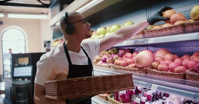 Man worker stocking the fruits in supermarket while listen to the music, side view