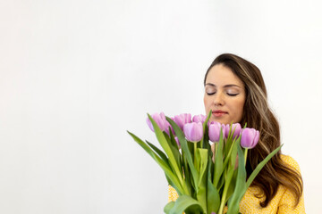 Beautiful happy woman with long hair with a bouquet of tulips in her hands on a white background. Sniffing the flowers. Copy space for text