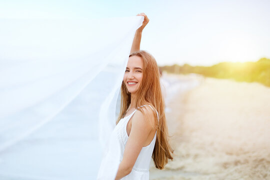 Happy smiling woman in free happiness bliss on ocean beach catching clouds. Portrait of a multicultural female model in white summer dress enjoying nature during travel holidays vacation outdoors.