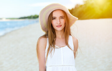 Portrait of a happy smiling woman in free happiness bliss on ocean beach standing with a hat. A female model in a white summer dress enjoying nature during travel holidays vacation outdoors.