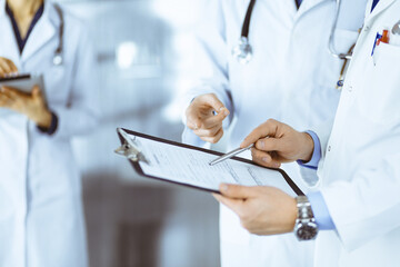 Unknown doctors, two men and a woman, discuss medical exam resoults, while standing at hospital office. Physicians using clipboards for filling up medication history records