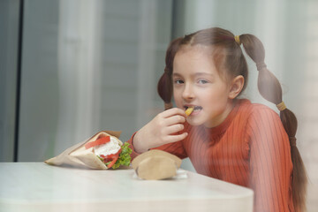 Cute little girl with ponytails eating souvlaki for lunch in Greek restaurant. Adroable white kid eats fries in Mediterranean cafe and looking in camera with a smile