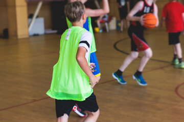 Fototapeta premium Junior teenage school team of kids children play basketball, players in the hall indoor venue court, sports team during the game, playing indoor match game on arena stadium on a wooden parquet floor