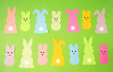 On a green background, funny Easter bunnies and pepps rabbits cut out of colored paper lie in a row, pattern.  Flat lay, top view.  The concept of children's creativity, application, crafts.