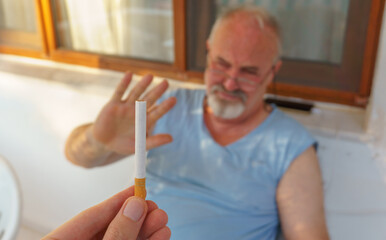 Elderly man refusing smoking cigarette offer at home. Quit smoking concept idea photo. 