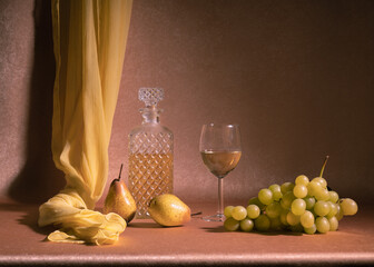.A carafe of white wine, next to a glass of white wine, two pears and a bunch of white grapes on an...