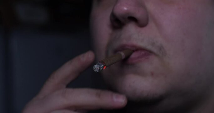 A man smokes a cigarette. Holding a cigarette between his fingers, the man takes a deep breath. Close-up. The concept of a bad habit of smoking.