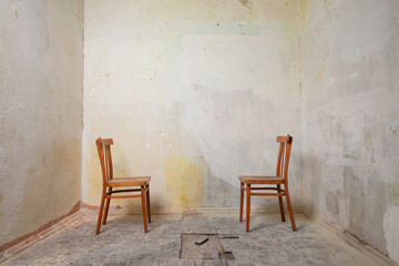 Two wooden chairs stand in an empty room without renovation