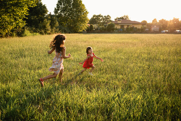 two girls in dresses running one after another in the evening field - Powered by Adobe
