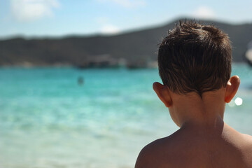 child boy with his back on the beach looking at the sea and mountains in the background on a vacation day