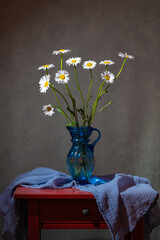 .Bouquet of pale daisies in a blue vase on a red table.
