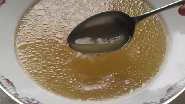 Stirring beef bone broth in a plate with a spoon, closeup