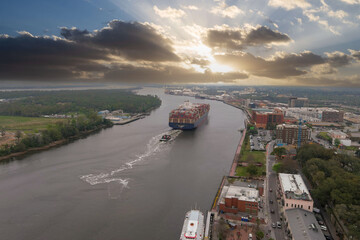 aerial shot of a container ship sailing along the Savannah River surrounded by hotels, office...