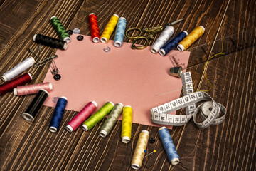a sewing still life with a plastic ruler, tape measure, assorted threads, golden vintage scissors on a brown wooden table with a sheet of pink colored paper