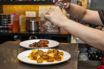 A waiter seasons Asian food before serving it to the tables of a Chinese restaurant