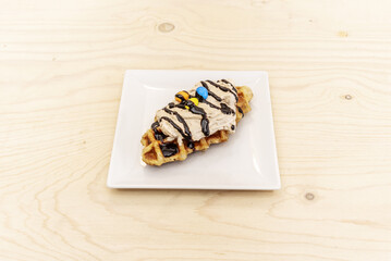 A waffle-style confection with chocolate syrup, cream and small colored chocolates