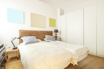 Bedroom with double beds, white wooden cabinets, beige bedspreads and light brown velvet headboard