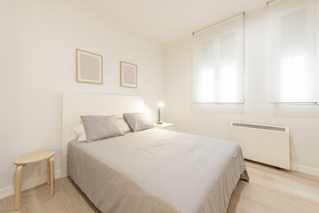 Fototapeta premium Bedroom with a double bed with wooden bedside tables, a gray bedspread with cushions, double windows with roller shutters and an electric heater