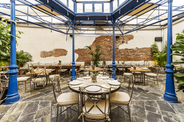 A restaurant dining room on a terrace with a blue painted metal pergola and slate floors
