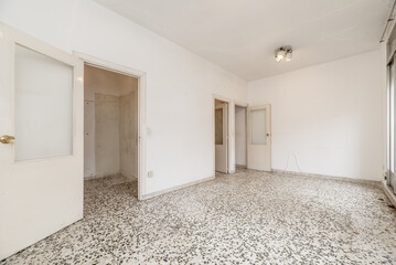 A room with plain white painted walls, terrazzo floors with black dots, and white wooden doors with glass