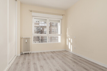 room with white aluminum windows with glass, a small cast iron radiator, a built-in wardrobe with white sliding doors and light wooden floors