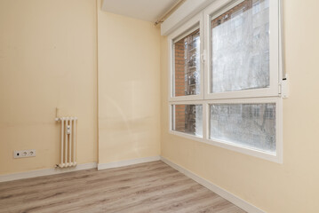 Corner of a room with white aluminum windows with dirty glass, small cast iron radiator and light...