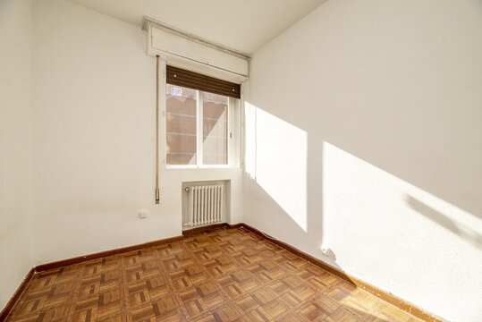 Room With white aluminum windows with glass, white painted walls, cast iron radiator in a niche and parquet-like sintasol floors