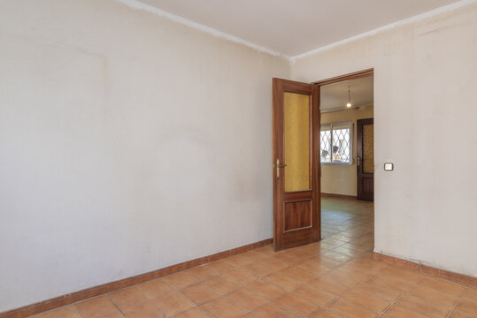 A small room with gotele walls and poorly painted white, brown stoneware floors and a sapele wood door with glass