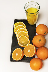 A few whole oranges, one halved, sliced on a slate plate and a glass of juice