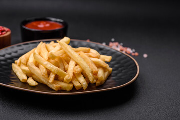 Delicious crispy french fries with salt and spices on a dark concrete background