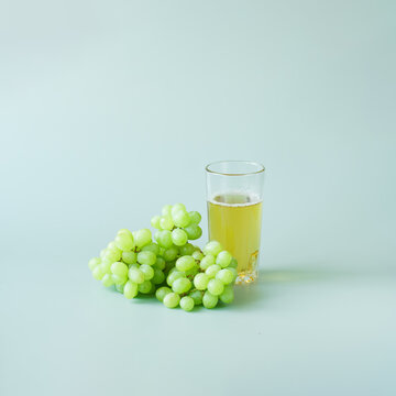 A bunch of white Japanese grapes next to a glass of light grape juice. Pastel green background