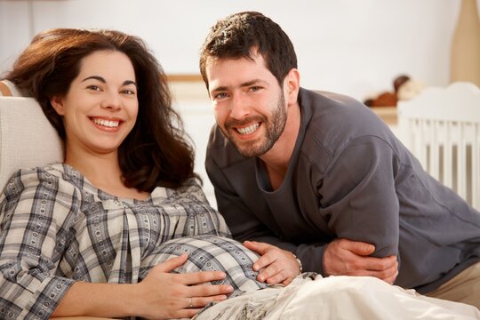 Happy pregnant woman and husband resting at home looking at camera similing.