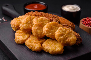 Delicious crispy chicken nuggets with salt and spices on a dark concrete background