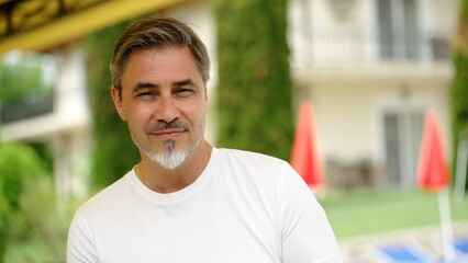 Portrait of happy middle aged man at home in front of house, confident, smiling. Outdoor in garden of villa, residence.