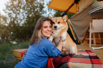 Happy young woman with Welsh Corgi Pembroke dog relaxing in glamping on summer day. Luxury camping tent for outdoor recreation and recreation. Lifestyle concept