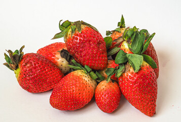 Lots of red strawberry berries with green leaves, a bit old