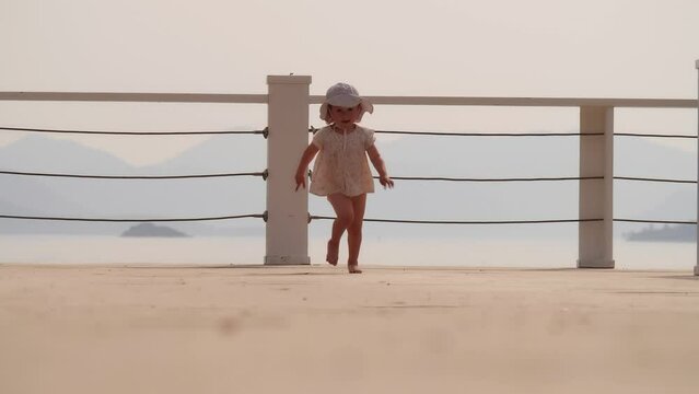 Cute little baby girl runs on the seaside pier on a sunny summer day, slow motion