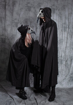 A gothic couple dressed as ravens, a black cape with a hood and a bird mask.