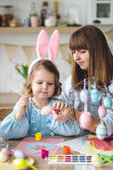 Beautiful mother and cute daughter are spending quality time together, making craft handmade eggs for Easter home decoration. Spring flowers, cozy holiday atmosphere , family traditions and values