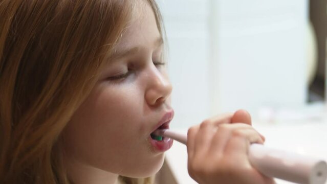 a little girl brushes her teeth with an electric toothbrush. 